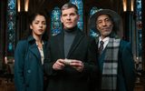 A man in a hat, a woman and another man holding a device stand in a church with candles