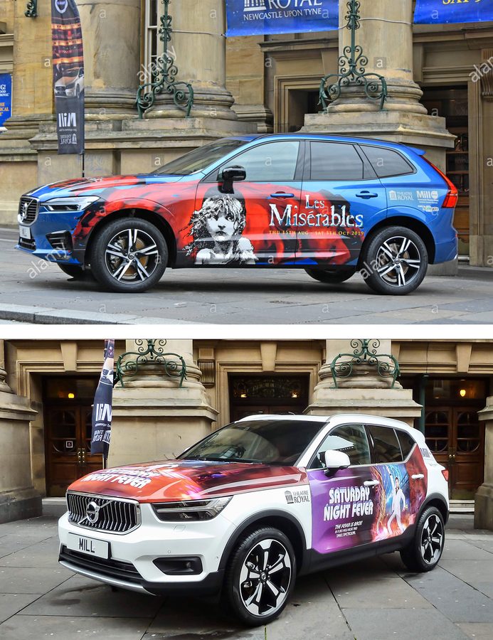 Two cars branded in show artwork stand outside the theatre