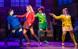 A young woman in a bright blue school woman is confronted by three fellow students, one dressed in red, one in green and another in yellow