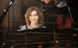 A woman is sat at a piano smiling