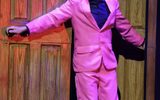 A man with black hair in a pink suit opens a door