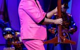 A man smiles in a pink suit too small for him holding a table with flowers