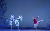 A female dancer stands in front of two dancers dressed as snow wolves