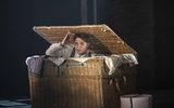 A boy pops out from his hiding place in a large wicker hamper