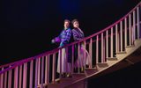 Two women stand back to back on a grand staircase