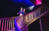 Two women stand back to back on a grand staircase