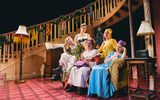 Five solemn looking women sit on a sofa in a festively decorated room