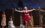 A woman in a red outfit stands with her arms outstretched and two other females look on