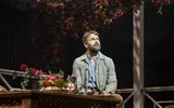 A man with a beard sits at a table covered with exotic flowers