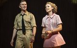 A man dressed in a military uniform smiles as he stands next to a woman dressed in a pink striped shirt and pink skirt