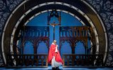 A man dressed in a red cloak and star shaped sunglasses stands in front of a alter