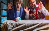 A boy and a man look surprised to find a giant eyeball lying on a bed