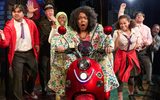 A surprised looking woman rides a red motorbike whilst a crowd of people look on