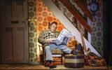 A dishevelled man sits on a old chair reading a newspaper