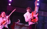 Members of a band dressed in white tuxedos and black bow ties play electric guitars