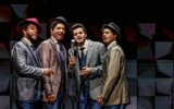 Four men standing behind microphones singing.