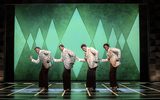 Four men dancing in matching outfits in front of a green background.