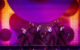 Four men in purple suits with their arms outstretched as they are dancing.