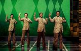 Four men dancing in matching outfits in front of a green background.