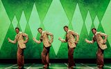 Four men dancing in matching outfits in front of a green background.