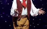 Clive Webb stands on stage wearing a red waistcoat and brown trousers.