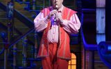 A male wearing a red waistcoat and shorts with a sailors hat playing the recorder.