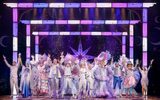 The full company of the pantomime stand smiling with their arms raised. They are all wearing silver outfits.