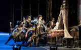 A group of gothicly dressed dancers surround an ornate four poster bed