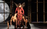 A frightening looking female dancer in a gothic red coat stands flanked by two loyal attendants