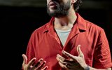 A man in a red shirt gestures with his hands.