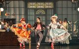 Three dancers, all in very extravagant and brightly coloured outfits dancing.