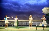 Four females all wearing tennis whites stand close to a tennis net.