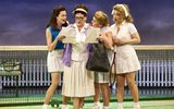 Four females all wearing tennis whites crowding around a piece of paper.