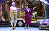 A male and female standing in front of a caravan as part of the set.