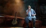 A man sings whist sitting beside a guitar.