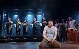 A man is on his knees as singers holding statue heads stand behind him.