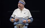 A male wearing a gym jacket and sweatbands around his head and wrists smiles.