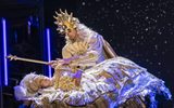 Two people dressed in golden outfits. The female is lying down whilst a male looks over her.
