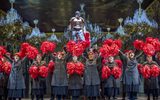 A large group of people wearing grey clothes hold red pom-poms above their heads.