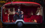 A female dressed all in black sits in a caravan decorated in red velvet.