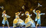 Cast members dressed in yellow and blue costumes, they are wearing sunflowers and carrying large bumble bees.