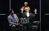 A female judge holds her hands in the air whilst a male in a suit is looking at her.