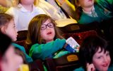 A girl wearing glasses is watching the stage and holding a packet of crisps.