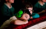 A boy gazes over the balcony wearing ear defenders.