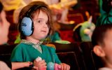 A young girl plays with her toys, wearing ear defenders.