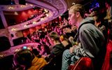 A young man sits in his seat looking out at the stage.