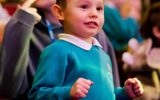 A young boy stands at his seat.