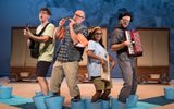 Four people standing with their feet inside blue buckets. They are all playing instruments.