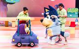A small cartoon dog sits in a purple coloured car; the dog is talking to a larger, blue dog.