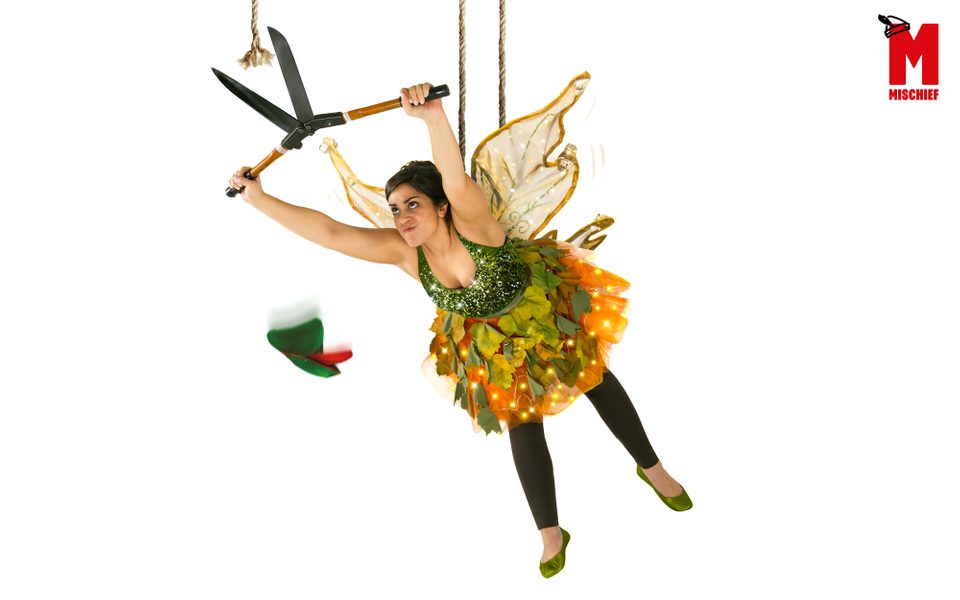 A woman dressed as a fairy hanging from a rope holds garden shears and cuts a rope.